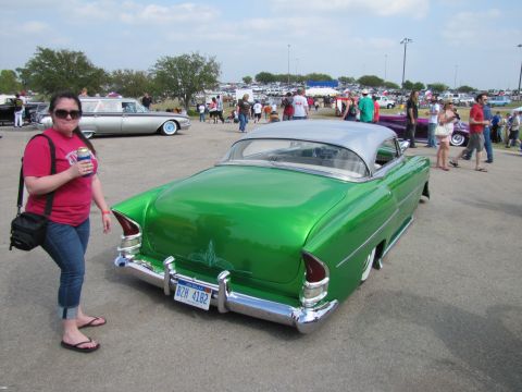 2006 BMW 5 Series - A woman stands next to a shiny green classic car with a silver roof at an outdoor car show.