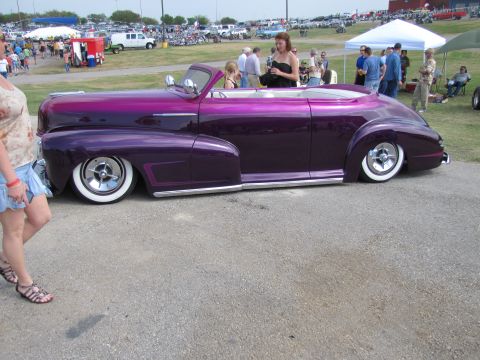 2006 BMW 5 Series - A low-slung, custom purple convertible is parked at an outdoor event with spectators milling about.