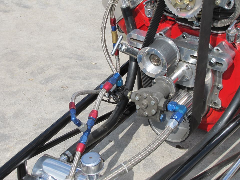 Engine with red block, silver pulleys, and braided fuel lines on concrete
