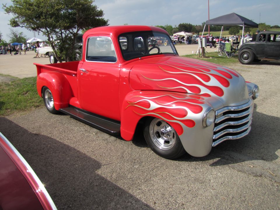 Red pickup truck with silver flames on the hood and fenders, lowered stance, chrome wheels
