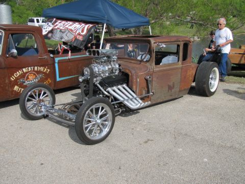 2006 BMW 5 Series - A heavily modified rat rod with a prominent V8 engine sits next to a vintage truck with custom lettering.