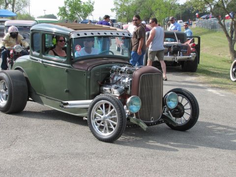 2006 BMW 5 Series - A custom hot rod with a prominent engine sits on a paved surface, with people and other vehicles in the background.