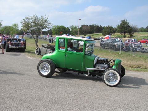 2006 BMW 5 Series - A green hot rod coupe is parked on the side of the road with other vehicles and people around.