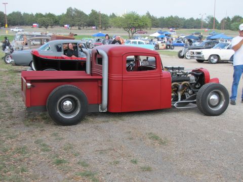 2006 BMW 5 Series - A custom red hot rod pickup truck is parked at an outdoor event with other vehicles in the background.