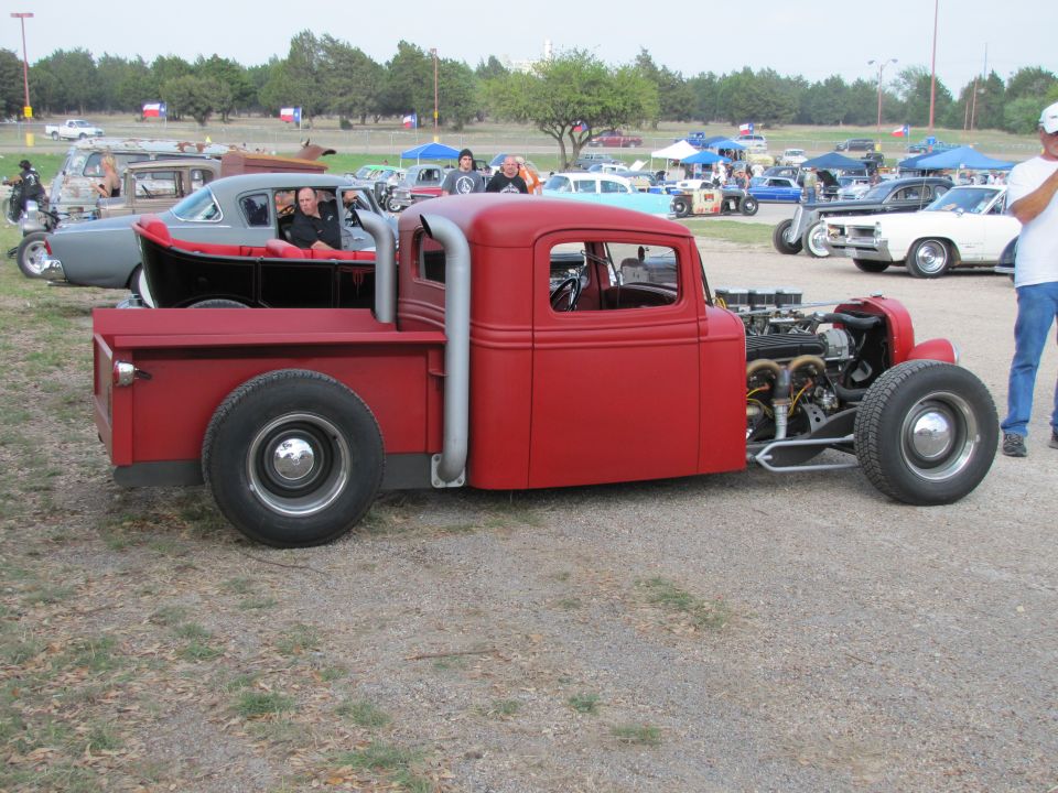 Red hot rod pickup truck with exposed engine and side pipes, viewed from the front three-quarter angle