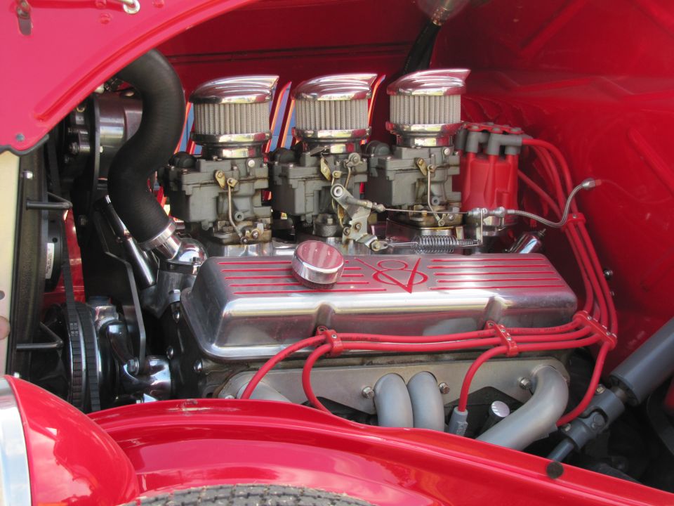 Close-up of a red hot rod engine with three carburetors and chrome valve covers