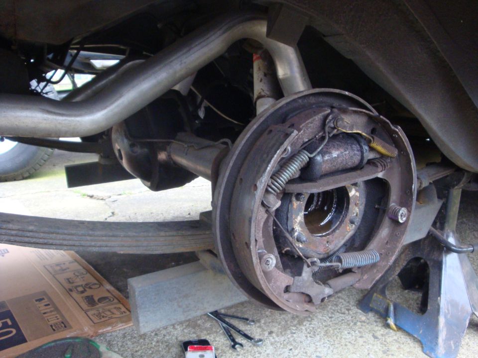Rear axle drum brake assembly with exhaust pipe and leaf spring