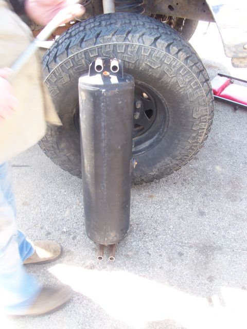 1989 Ford Bronco - This exhaust muffler has been decorated to resemble a penguin, positioned near a vehicle's tire.
