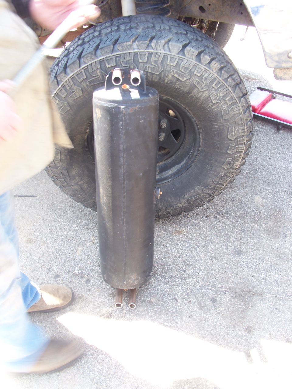 Exhaust muffler painted to look like a penguin, placed in front of a large off-road tire