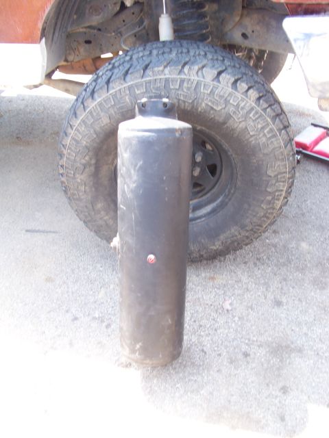 1989 Ford Bronco - A propane tank is positioned in front of the rear tire and suspension of a vehicle.