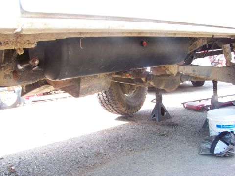 1989 Ford Bronco - The underside of a vehicle is visible, with a large black fuel tank and suspension parts.