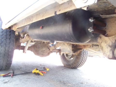 1989 Ford Bronco - Close-up of an auxiliary tank installed on the undercarriage of a vehicle, showing suspension and drivetrain parts.