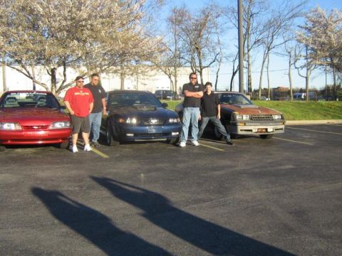 2007 Ford Mustang - A red 1994 Ford Mustang convertible is parked next to a blue Mustang and a brown car, with four men standing nearby.
