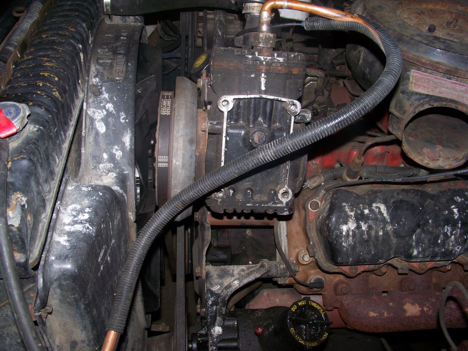 Engine bay with visible belts, pulleys, and engine block. Some hoses and a black compressor unit are also present