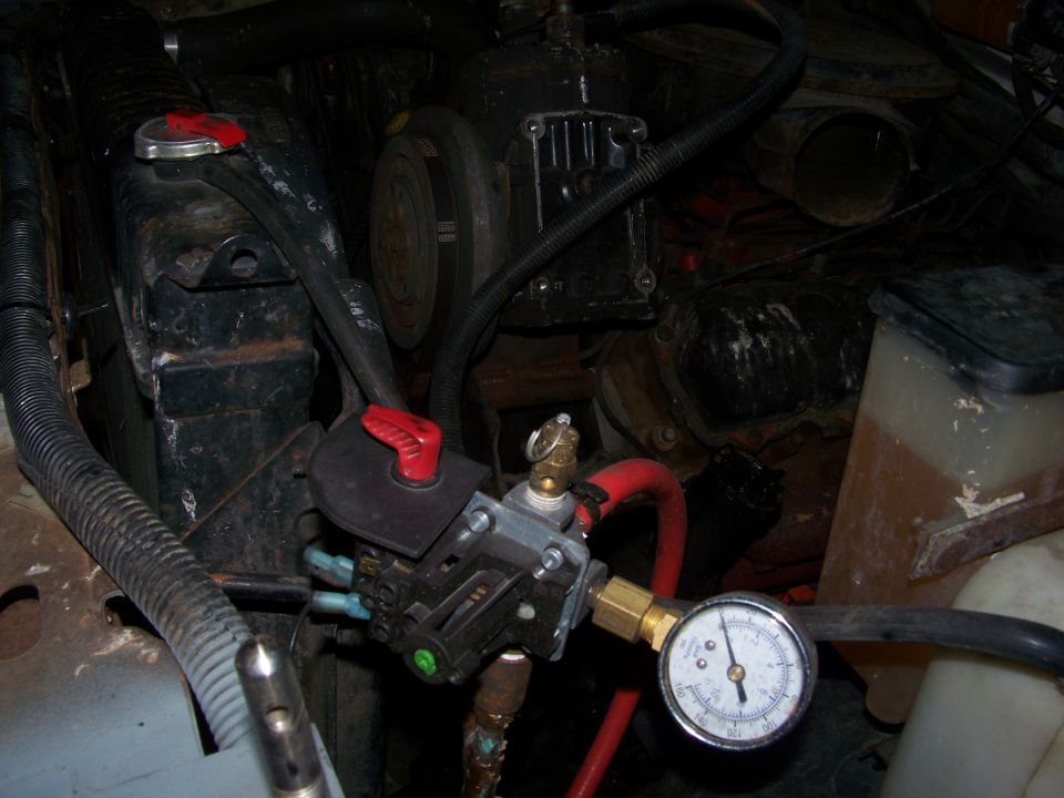 Engine bay showing a pressure gauge connected to a valve assembly near the radiator