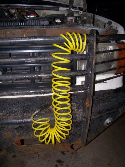 1989 Ford Bronco - A yellow air hose is coiled and hanging from the front grille of a truck, obscuring the view of the radiator.