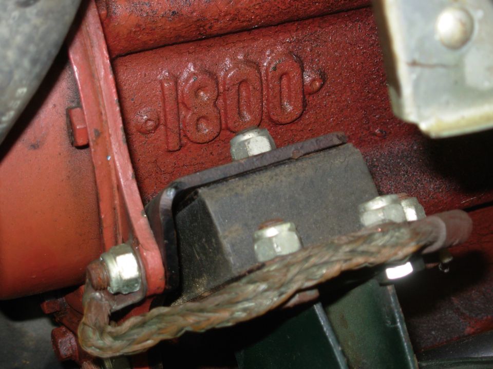 Red engine block cast with '1800' above a black engine mount, bolts, and braided ground strap