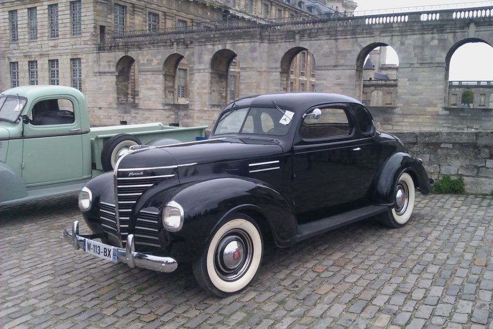 Black 1939 Plymouth coupe with whitewall tires on cobblestones by a stone arcade