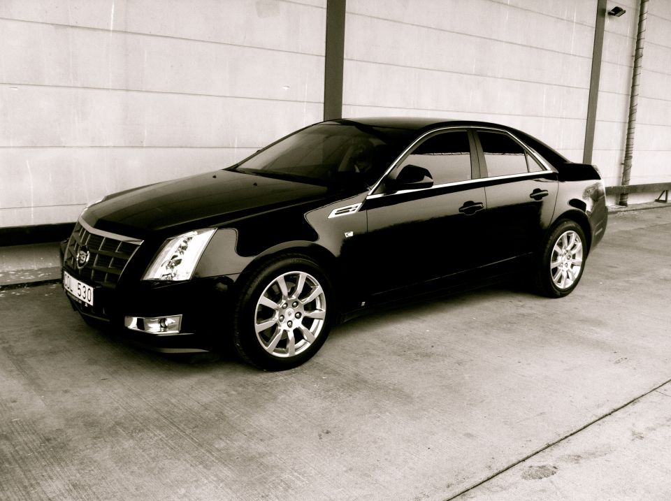 Black Cadillac CTS sedan parked at 3/4 front angle by concrete wall