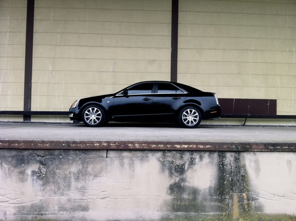 Black sedan shown in side profile parked by a beige wall on a concrete ledge.