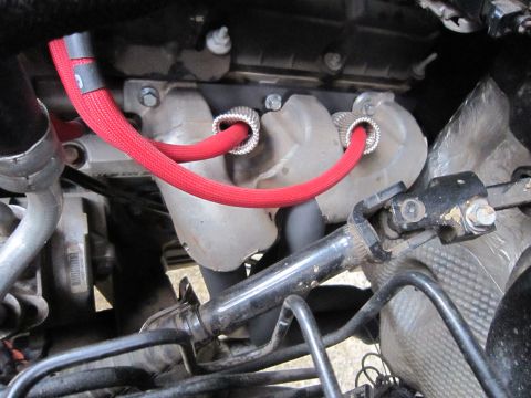 2008 Jeep Wrangler - Close-up under the hood showing red braided-sleeve spark plug wires with silver heat-shield boots routed down past a cast exhaust manifold…