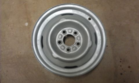 1965 Ford Mustang - A single silver steel wheel is shown against a brown surface.