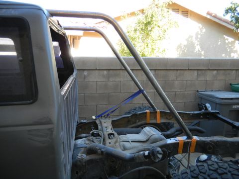 1997 Ford Ranger - A bare-metal roll bar hoop is being mock-fitted behind the cab of a stripped tan pickup, held in place with a blue ratchet strap and orange…