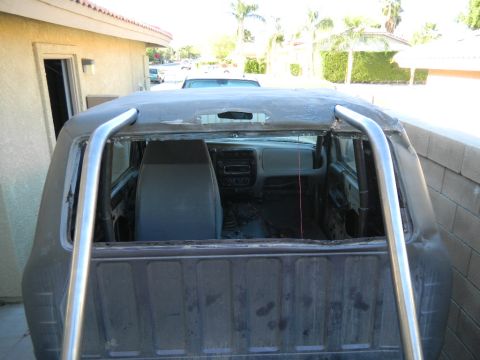 1997 Ford Ranger - Rear view looking forward into a gutted pickup cab with the rear window glass and roof skin cut out, bare-metal roll bar tubing running up…