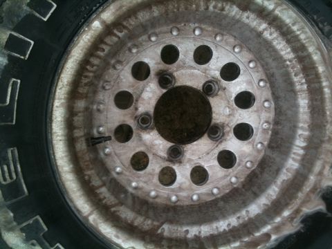 1993 Ford Bronco - A close-up view of a weathered wheel and tire, showing the tire's tread pattern and the wheel's lug nut holes.
