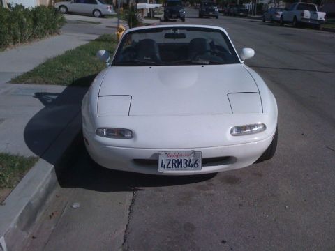 1991 Mazda Miata - This white convertible sports car is parked on a residential street with its pop-up headlights down.