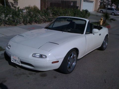 1991 Mazda Miata - A white convertible sports car with pop-up headlights is parked on a street.