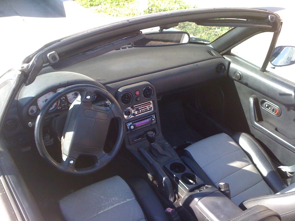 Interior of a 1991 Mazda Miata with a black steering wheel, gray seats, and an aftermarket stereo