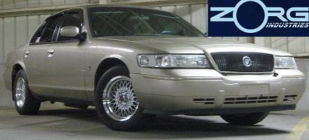 2000 Mercury Grand Marquis - A gold 2000 Mercury Grand Marquis sedan is parked indoors, showing its front grille and aftermarket wheels.