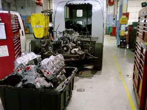 1989 Ford Bronco - A workshop scene shows a vehicle chassis with its engine bay exposed and a bin of engines in the foreground.