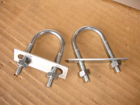 1993 Ford Taurus - Two U-bolts with mounting plates and nuts are shown against a wooden background.