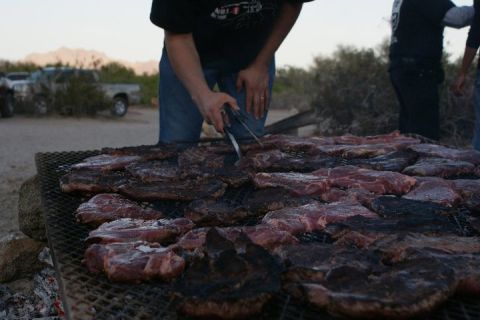1987 Ford Bronco - A group of people are gathered around a large grill, cooking a substantial amount of meat in an outdoor setting.