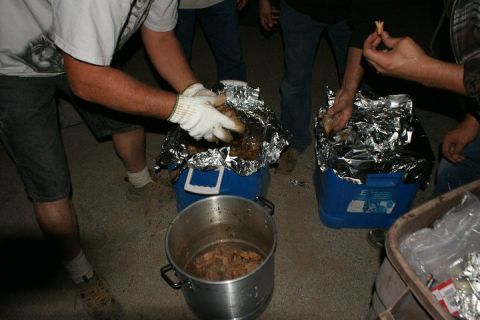 1987 Ford Bronco - Several people are gathered around, preparing and handling food that is wrapped in aluminum foil.