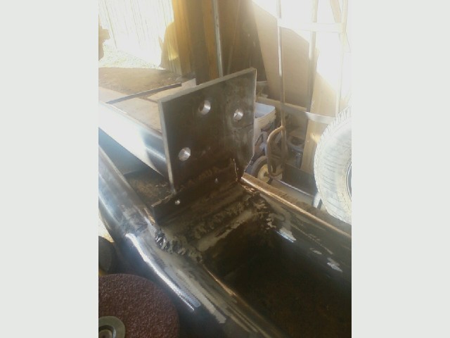 Metal bracket with three bolt holes welded to a frame section. Grinding disc visible