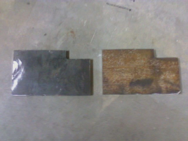 two metal brackets, one dark and one rusty, on a flat surface