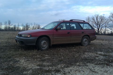 1998 Subaru Legacy - Red 1998 Subaru Legacy wagon sits in a muddy field under a cloudy sky.
