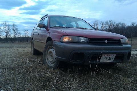1998 Subaru Legacy - A red 1998 Subaru Outback wagon sits in a field under a cloudy sky.