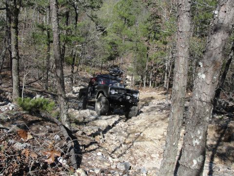 1967 Ford Mustang - Off-road vehicle driving on a rough, rocky path in a forest. Another vehicle follows.