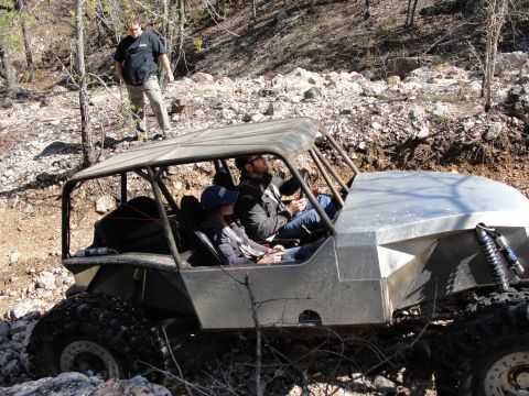 1967 Ford Mustang - An off-road buggy navigates a rocky trail with two occupants inside and a person standing on the roof.
