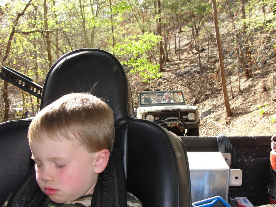Sleeping child in foreground, 1970s Ford Bronco on dirt road behind. Off-road scene
