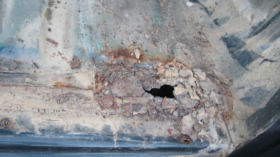 Heavily rusted and corroded vehicle floor pan with a large hole