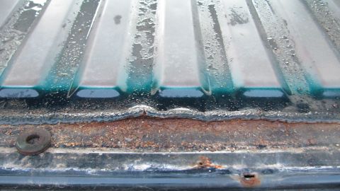 1992 Ford Bronco - Close-up of a rusted tailgate edge, with teal paint visible beneath the corrosion.