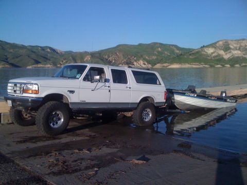 1996 Ford C-350 (Centurion Conversions) - A lifted Ford Bronco SUV is used to launch a boat into a calm lake on a sunny day.
