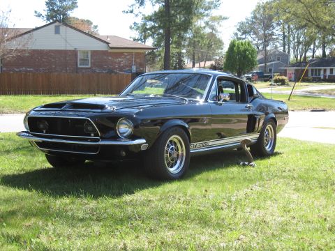 1968 Shelby GT500 - A classic black 1968 Shelby GT500 is parked on a grassy lawn, with houses and trees in the background.