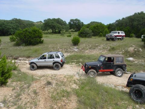 1973 Ford Bronco - Multiple off-road vehicles navigate a dirt path through a natural landscape.