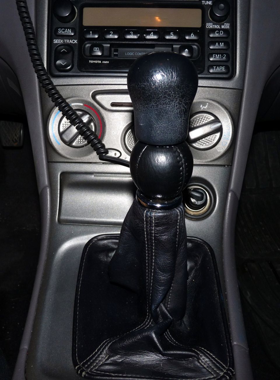 Car interior showing gear shift, radio, and climate controls. Toyota logo visible on radio